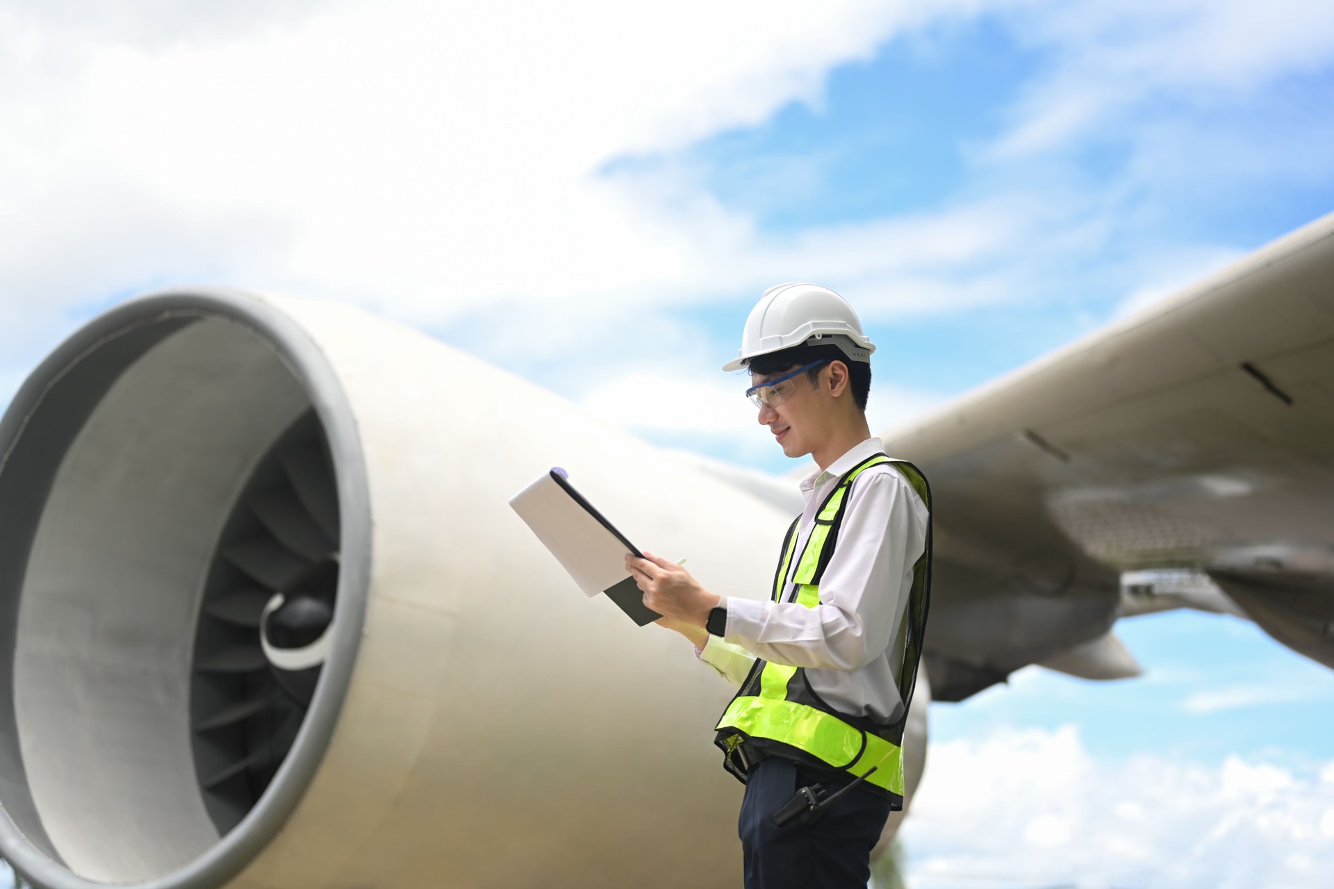 Young aviation engineer or inspector standing in front of a large airplane engine checking data on digital tablet