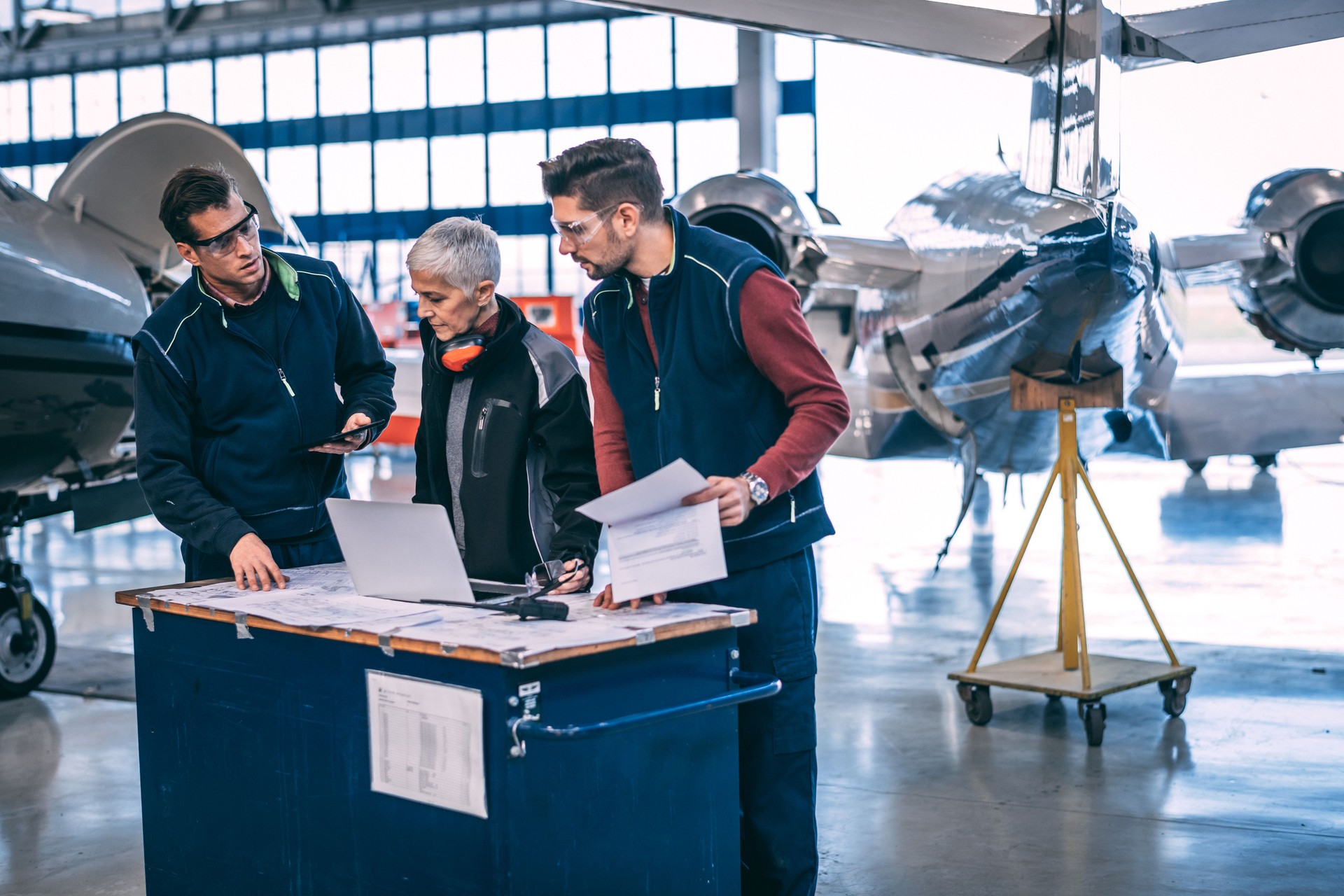 Elderly female aircraft engineer coordinating with her crew of mechanics in an airplane hangar